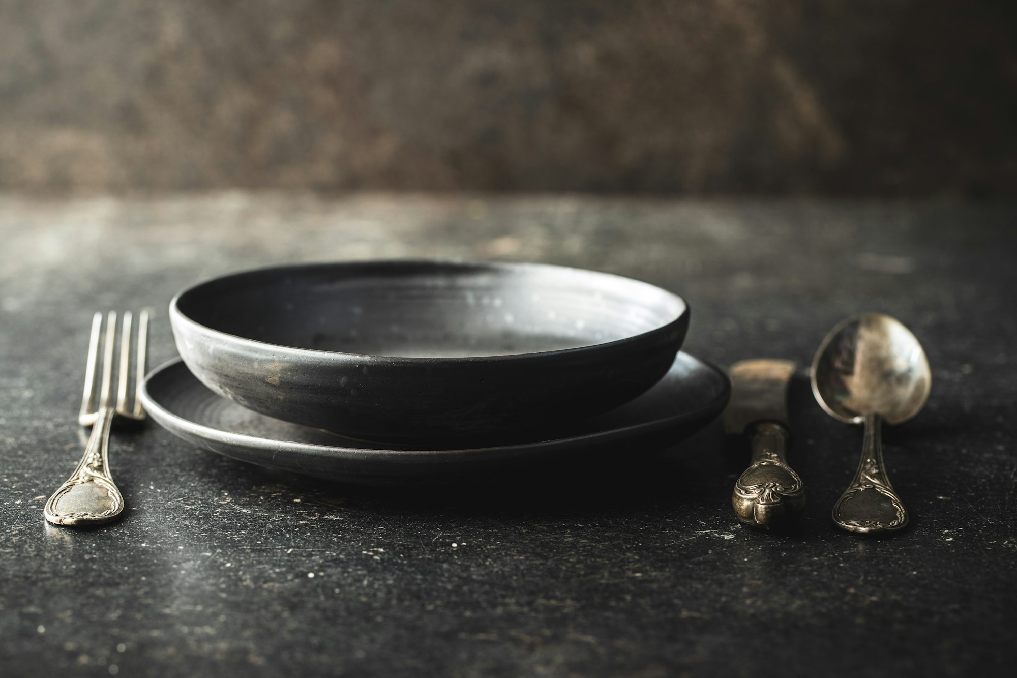 Empty vintage plate with silver knife, spoon and fork on black table.